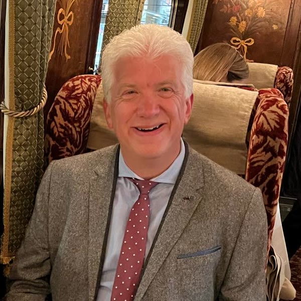 Andy, smiling, in a suit and red tie